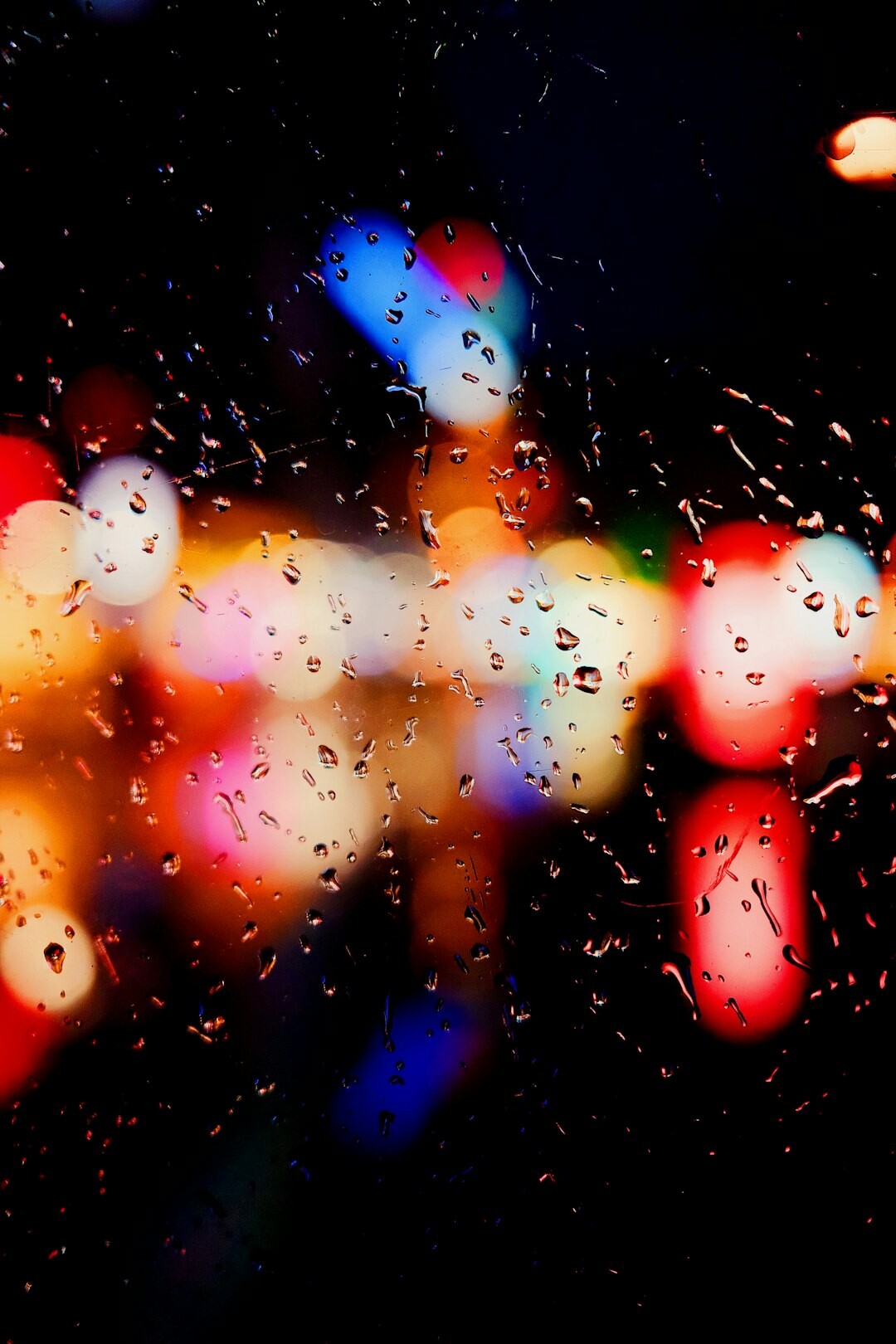 Rain drops on a window with blurred city lights at night