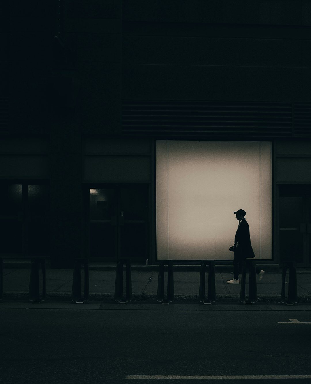 Silhouette of a detective in a coat and hat standing under a streetlamp